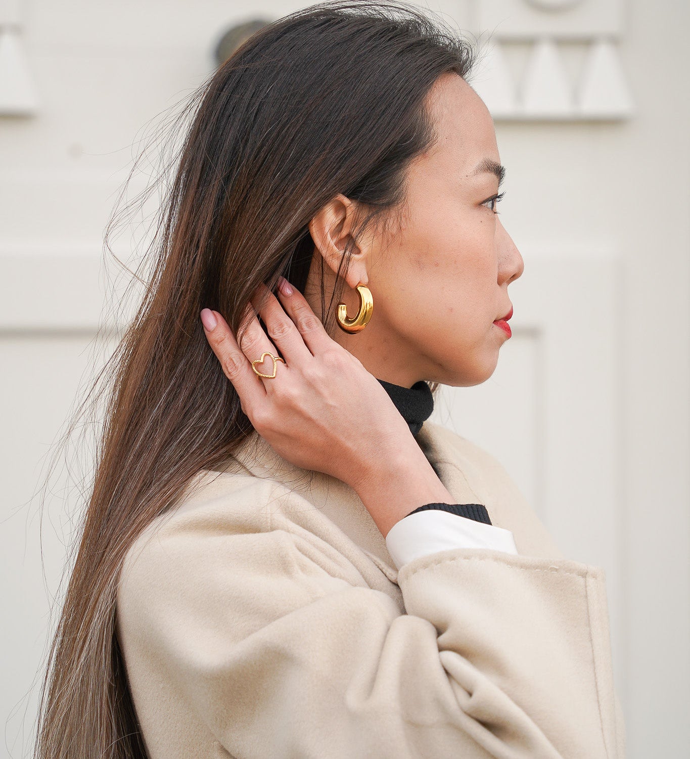 Jeune femme se tenant les cheveux, portant une bague en forme de cœur et une paire de boucles d’oreilles en acier inoxydable, mettant en valeur des bijoux modernes et élégants.