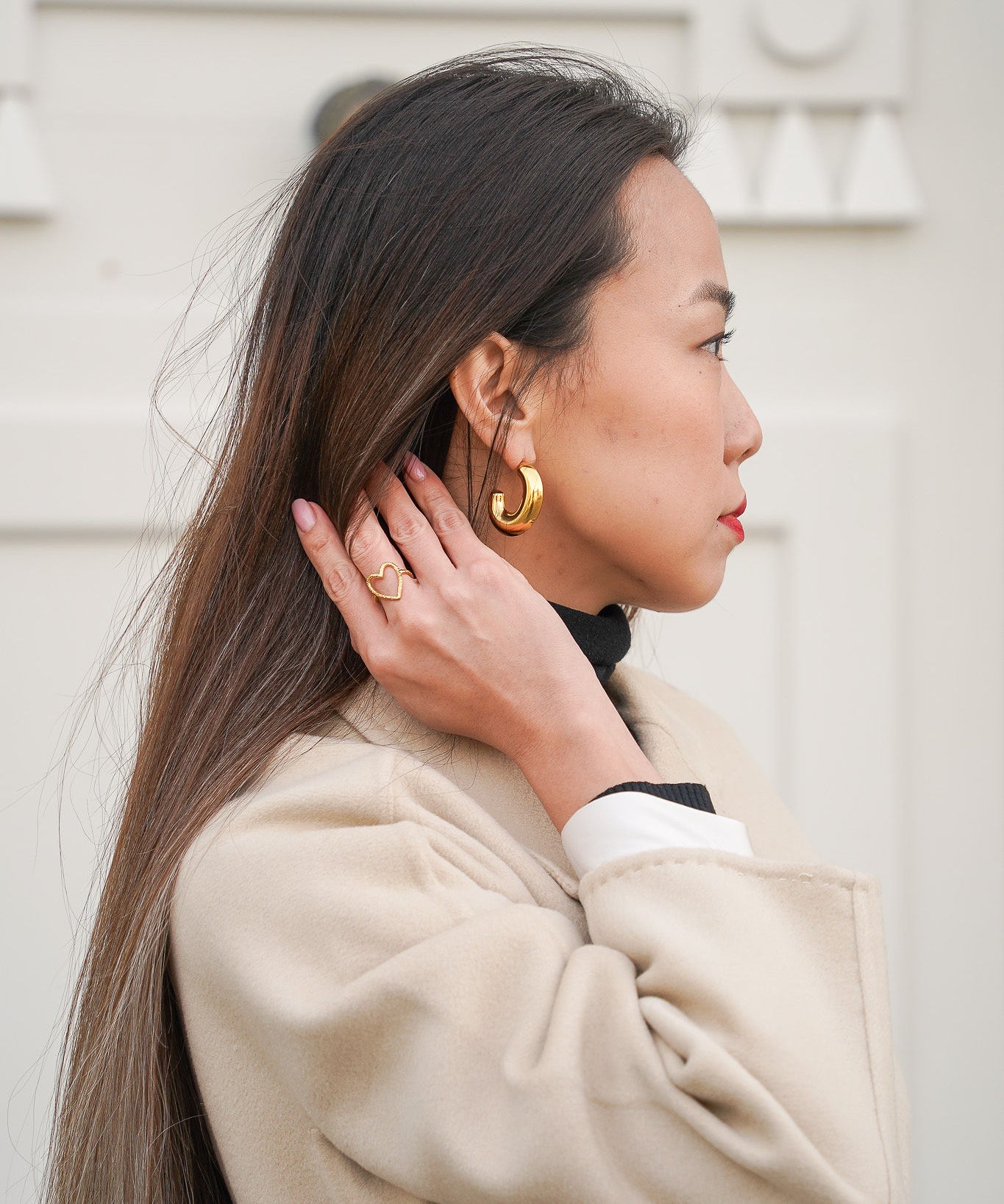 Jeune femme se tenant les cheveux, portant une bague en forme de cœur et une paire de boucles d’oreilles en acier inoxydable, mettant en valeur des bijoux modernes et élégants.