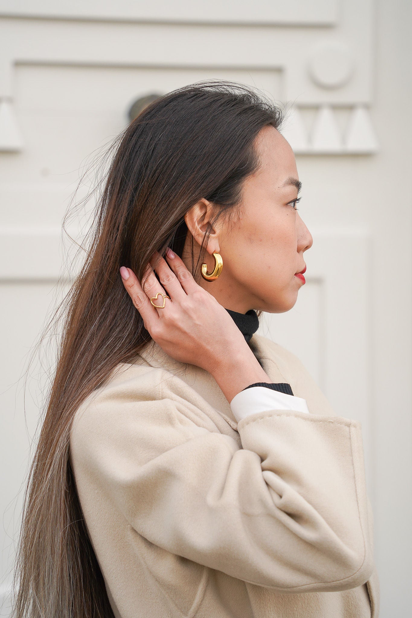 Jeune femme se tenant les cheveux, portant une bague en forme de cœur et une paire de boucles d’oreilles en acier inoxydable, mettant en valeur des bijoux modernes et élégants.