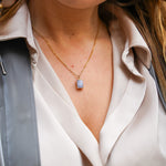 Jeune femme se tenant les cheveux, portant un collier en acier inoxydable avec un pendentif bleu, ajoutant une touche élégante et colorée à son look. Cadeau pour la Saint-Valentin