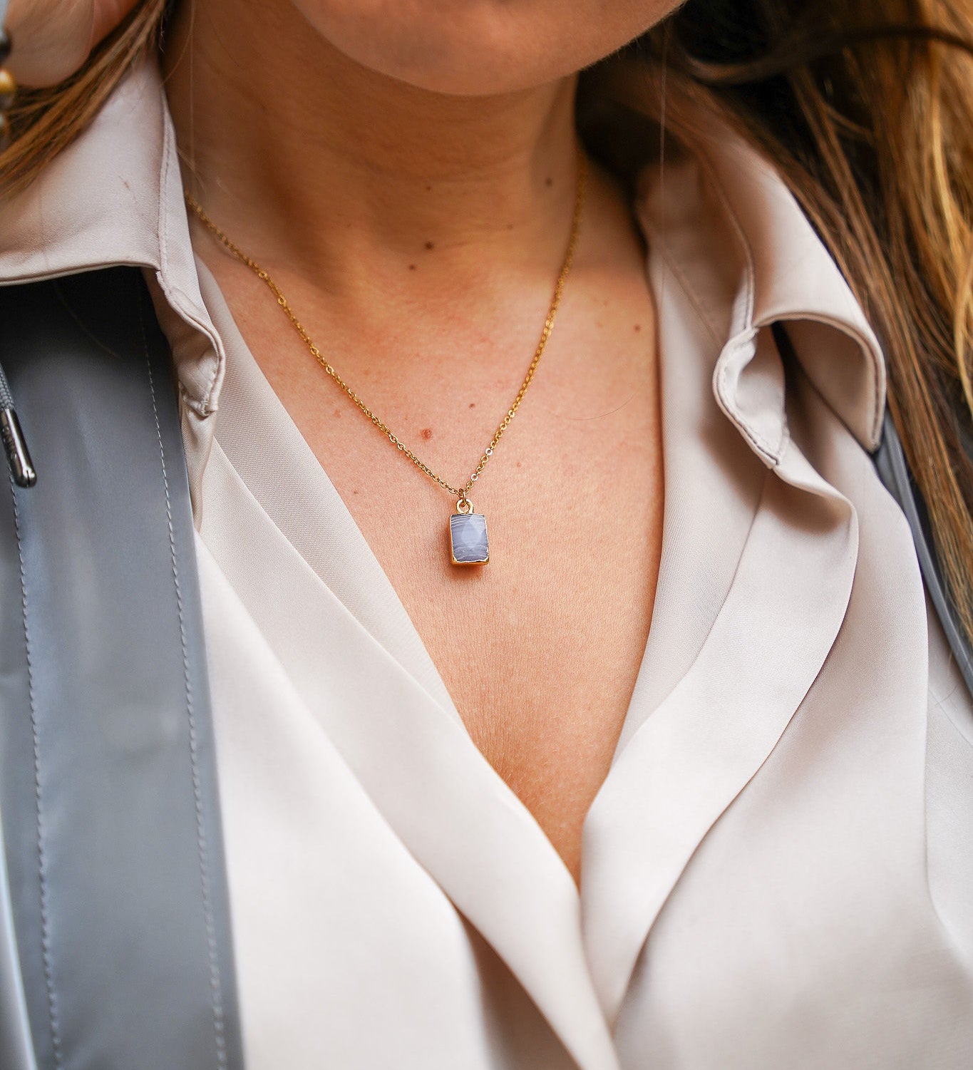 Jeune femme se tenant les cheveux, portant un collier en acier inoxydable avec un pendentif bleu, ajoutant une touche élégante et colorée à son look. Cadeau pour la Saint-Valentin