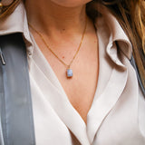 Jeune femme se tenant les cheveux, portant un collier en acier inoxydable avec un pendentif bleu, ajoutant une touche élégante et colorée à son look. Cadeau pour la Saint-Valentin