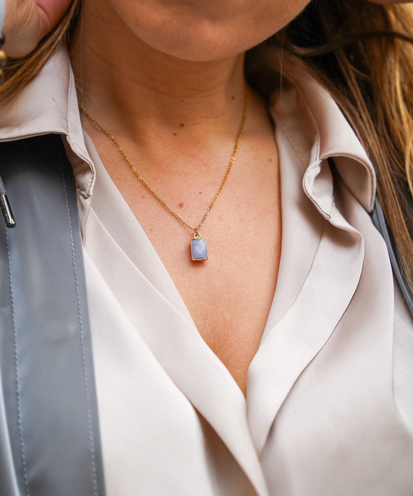 Jeune femme se tenant les cheveux, portant un collier en acier inoxydable avec un pendentif bleu, ajoutant une touche élégante et colorée à son look. Cadeau pour la Saint-Valentin