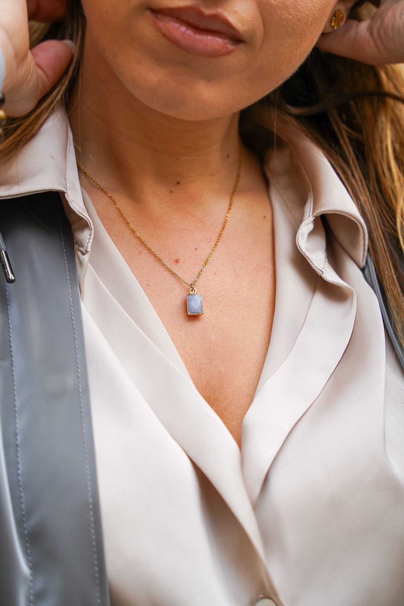 Jeune femme se tenant les cheveux, portant un collier en acier inoxydable avec un pendentif bleu, ajoutant une touche élégante et colorée à son look. Cadeau pour la Saint-Valentin