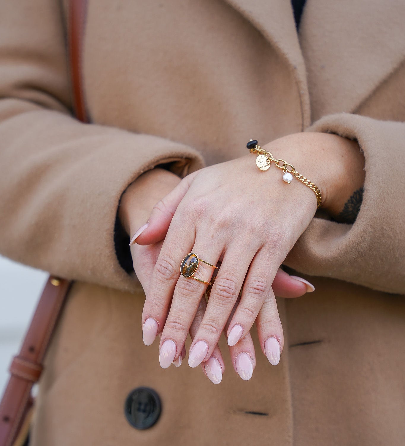 Zoom sur les mains d'une femme portant une bague en acier inoxydable avec une pierre en œil de tigre et un bracelet à breloques en nacre et noir, combinant élégance et style unique.