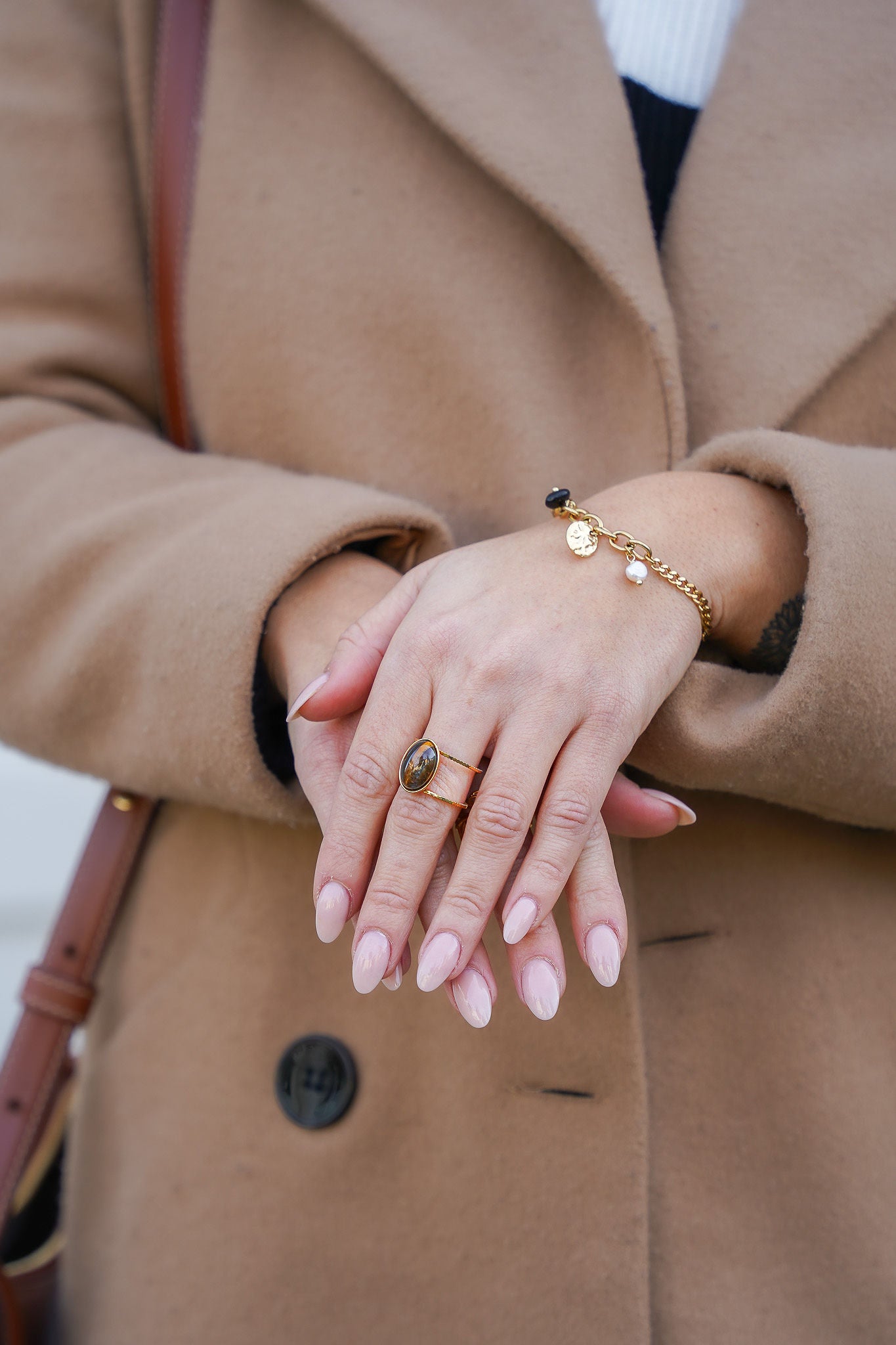 Zoom sur les mains d'une femme portant une bague en acier inoxydable avec une pierre en œil de tigre et un bracelet à breloques en nacre et noir, combinant élégance et style unique.